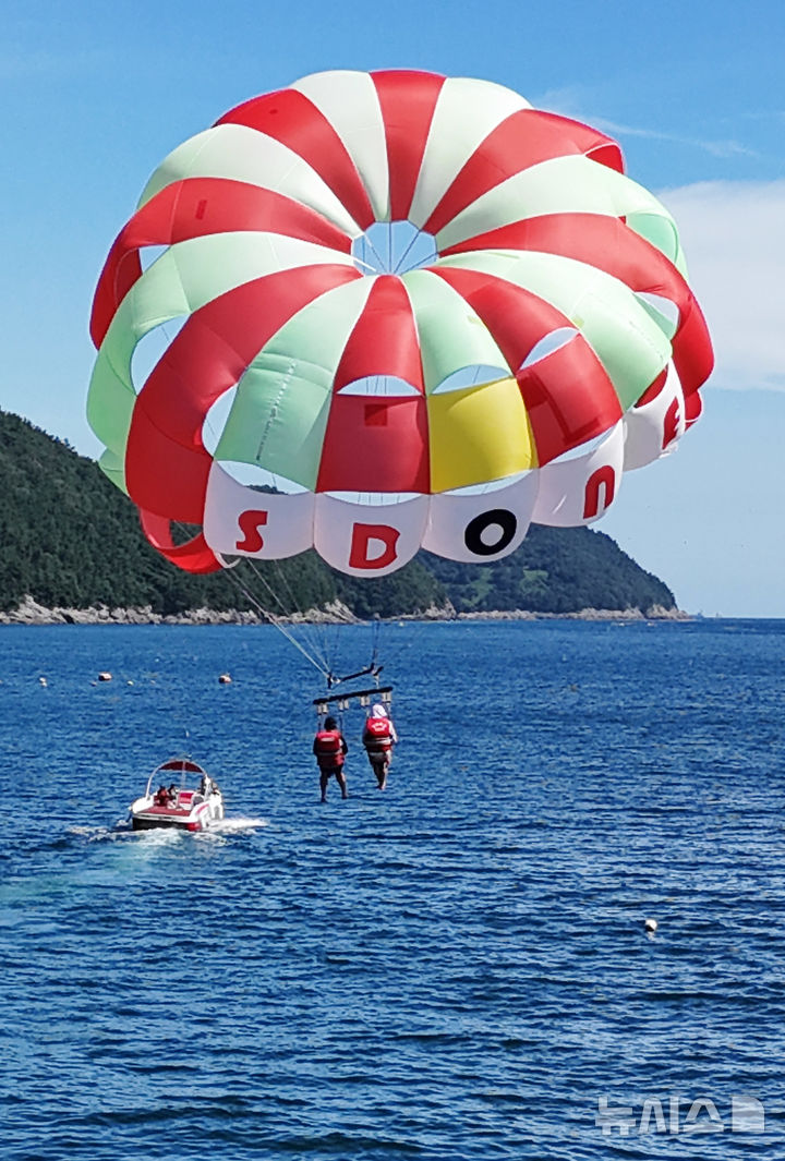 [남해=뉴시스] 차용현 기자 = 전국 대부분 지역에 폭염경보가 내려진 30일 오후 경남 남해군 원천마을 인근 해안에서 피서객들이 페러세일링을 타고 하늘을 날으며 더위를 식히고 있다. 2025.07.30. 2025.07.30.con@newsis.com