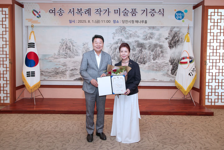 [당진=뉴시스] 여송 서복례(오른쪽) 화백이 1일 당진시청 해나루홀을 찾아 오성환 시장에게 수해 피해로 어려움을 겪고 있는 시민들을 응원하기 위해 작품 '왜목마을 시목 소나무'를 기탁한 후 기념 사진을 찍고 있다. (사진=당진시 제공) 2025.08.01. photo@newsis.com *재판매 및 DB 금지