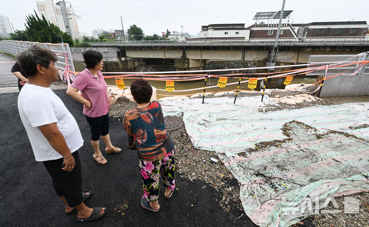 [광주=뉴시스] 이영주 기자 = 4일 오전 광주 북구 신안동 서암대로 100번길 주변 무너진 투명홍수방어벽 주변으로 주민들이 모여 있다. 주민들은 지난달 17일 426㎜ 폭우가 쏟아졌을 당시 투명홍수방어벽이 물그릇 역할을 하면서 마을이 침수됐다고 주장, 당국을 상대로 소송에 나설 방침이다. 2025.08.04. leey2578@newsis.com