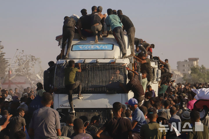 [라파=AP/뉴시스] 4일(현지 시간) 가자지구 남부 라파 인근 모라그 회랑을 따라 이동하는 인도주의 구호 물품 수송 트럭에 음식과 지원 물품을 받으려는 팔레스타인 주민들이 몰려들고 있다. 2025.08.05.