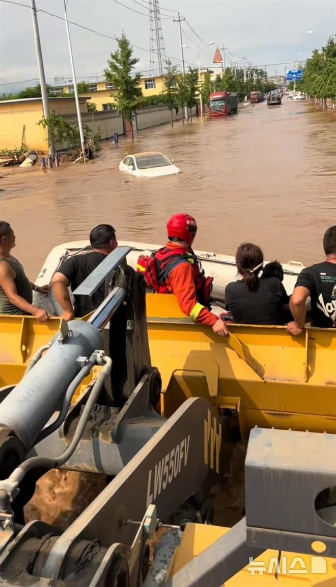  [뉴시스] 중국 베이징 홍수로 고립된 주민들이 한 남성이 몰고 온 굴삭기 삽에 올라타 구조되는 모습.(사진=지무뉴스) 