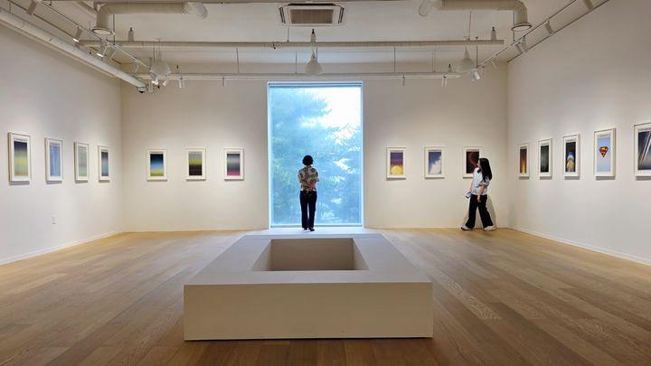 [사진=박현주 미술전문기자]3전시실에 선보인 쇼 시부야의 작품. '뉴욕 타임스' 신문 36점이 질서 있게 걸려 있다. 한쪽 벽면에는 총격 사건과 전쟁, 재난과 참사의 소식들이 압축된 색면으로 기록되어 있고, 마주한 벽면에는 같은 날 아침의 광활하고 고요한 하늘 풍경이 펼쳐진다. 관객은 힌지로 설치된 액자를 넘기며 채색된 화면과 원본 신문을 번갈아 볼수 있다. *재판매 및 DB 금지