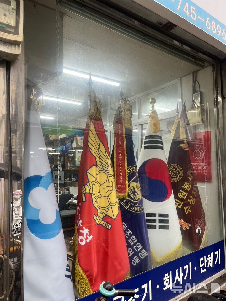 [서울=뉴시스]유서영 인턴기자=서울 종로구 관수동 휘장골목의 한 휘장 전문업체 진열창. 태극기를 비롯해 군기, 단체기 등 다양한 깃발이 나란히 걸려 있다. 2025.08.14