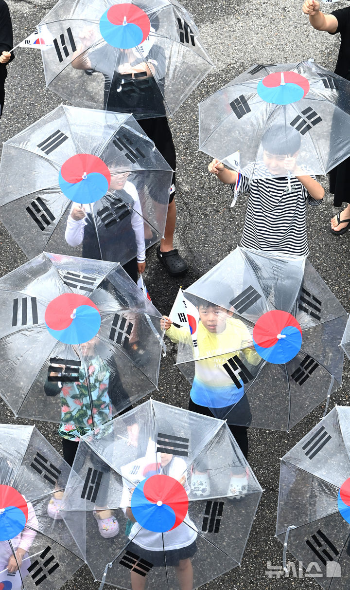 [수원=뉴시스] 김종택 기자 = 제80주년 광복절을 하루 앞둔 14일 경기 수원시 세류1동 행정복지센터에서 세류1동 새마을문고 '책먹는 아이들' 어린이들이 태극기 우산을 쓰고 만세삼창을 외치고 있다. 2025.08.14. jtk@newsis.com