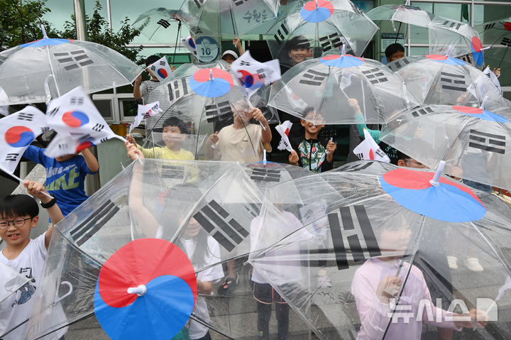 [수원=뉴시스] 김종택 기자 = 제80주년 광복절을 하루 앞둔 14일 경기 수원시 세류1동 행정복지센터에서 세류1동 새마을문고 '책먹는 아이들' 어린이들이 태극기 우산을 쓰고 만세삼창을 외치고 있다. 2025.08.14. jtk@newsis.com