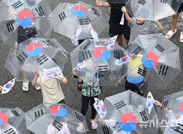 [수원=뉴시스] 김종택 기자 = 제80주년 광복절을 하루 앞둔 14일 경기 수원시 세류1동 행정복지센터에서 세류1동 새마을문고 '책먹는 아이들' 어린이들이 태극기 우산을 쓰고 만세삼창을 외치고 있다. 2025.08.14. jtk@newsis.com
