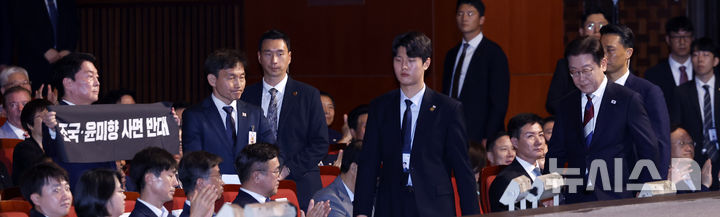 [서울=뉴시스] 최동준 기자 = 이재명 대통령이 15일 서울 종로구 세종문화회관에서 열린 제80주년 광복절 경축식에서 경축사를 마치고 이동하고 있는 가운데 안철수 국민의힘 당대표후보가 조국, 윤미향 사면 반대 피켓을 들고 있다. 2025.08.15. photocdj@newsis.com