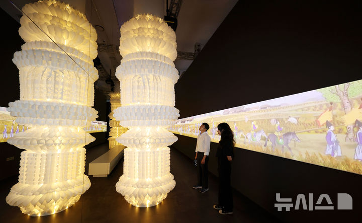 [서울=뉴시스] 홍효식 기자 = 19일 서울 중구 동대문디자인플라자(DDP)에서 열린 '헤리티지 : 더 퓨처 판타지' 전시 기자간담회에서 국가유산진흥원 직원들이 조선 왕실의 행차 풍경인 '환어행렬도' 미디어아트를 배경으로 한지를 활용한 '귀환의 메아리' 작품을 살펴보고 있다.국내 최초 국가유산을 활용한 디지털 콘텐츠 종합 전시 '헤리티지 : 더 퓨처 판타지'는 오는 23일 개막해 9월 17일까지 열린다. 2025.08.19. yesphoto@newsis.com