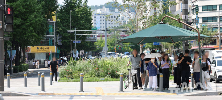 [서울=뉴시스] 권창회 기자 = 전국 대부분 지역에 폭염특보가 발효된 21일 서울 종로구 광화문광장 인근에서 시민들이 그늘막 아래서 햇빛을 피하며 신호를 기다리고 있다. 2025.08.21. kch0523@newsis.com