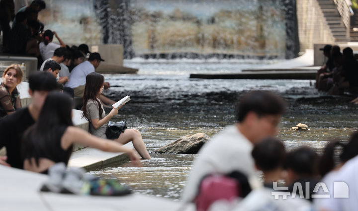 [서울=뉴시스] 김명원 기자 = 지난 24일 서울 중구 청계천에서 한 시민이 이어지는 더위를 식히며 책을 읽고 있다. 2025.08.24. kmx1105@newsis.com