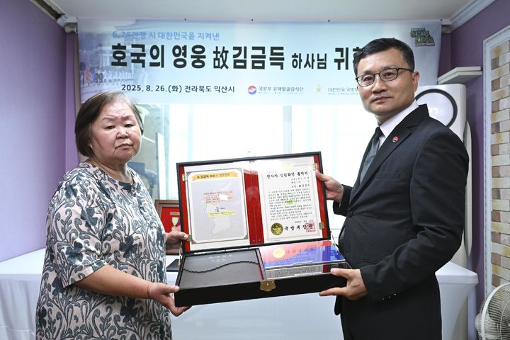 [서울=뉴시스] 26일 유가족 대표인 고인의 외동딸 김순임 씨(71)가 이근원 국방부유해발굴감식단장으로부터 '호국의 얼 함'을 전달받은 후 기념사진을 촬영하고 있다. 함 내부에는 고인의 유해와 함께 발굴된 인식표가 담겨 있다. (사진=국방부 제공) 2025.08.26. photo@newsis.com *재판매 및 DB 금지