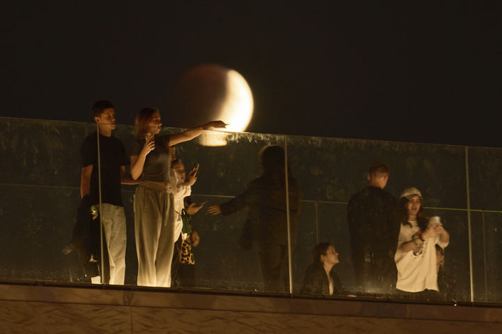 [모스크바=AP/뉴시스] 7일(현지 시간) 러시아 모스크바 자랴디예 공원에서 시민들이 산책을 즐기는 동안 개기월식이 진행되고 있다. '개기월식'은 달이 지구 그림자에 완전히 가려지는 천문 현상이다. 2025.09.08.