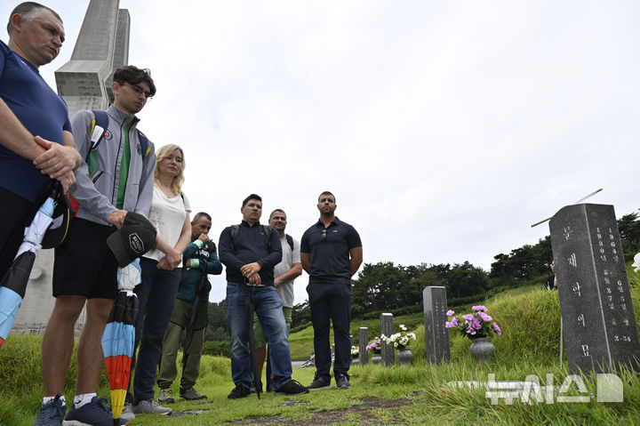 [광주=뉴시스] 박기웅 기자 = 2025 광주현대세계양궁선수권대회 출전 선수단 대상 팸투어 프로그램에 참여한 리투아니아와 헝가리 선수단이 9일 오전 국립5·18민주묘지를 방문, 문재학 열사 묘 앞에서 해설사의 설명을 듣고 있다. 2025.09.09. pboxer@newsis.com