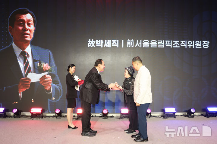 [서울=뉴시스]고(故) 박세직 서울올림픽조직위원장의 부인 홍숙자 여사(오른쪽에서 두 번째)가 고인을 대신해 하형주 국민체육진흥공단 이사장(왼쪽에서 두 번째)으로부터 공로패를 받고 있다. (사진=국민체육진흥공단 제공)