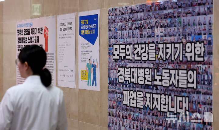 [대구=뉴시스] 이무열 기자 = 경북대학교병원 노조에 소속된 간호사와 간호조무사, 청소·돌봄 등 노동자들이 인력 충원 등을 요구하며 전국 3개 국립대병원 노조와 공동 파업에 들어갔다. 사진은 17일 대구 중구 경북대학교 병원 복도에 붙은 공공운수노조 의료연대본부 대자보 앞으로 의료진이 이동하는 모습. 2025.09.17. lmy@newsis.com