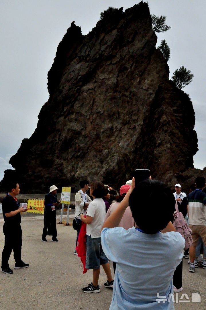 [서울=뉴시스] '2025 독도탐방' 참가자가 울릉도 통구미 거북바위를 바라보며 사진을 찍는 모습. 