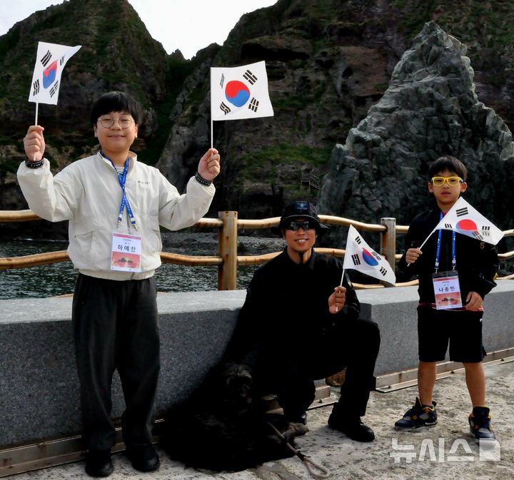 [서울=뉴시스] '2025 독도탐방' 참가자들이 독도경비대 대원과 독도 마스코트인 삽살개와 기념사진을 찍는 모습. 