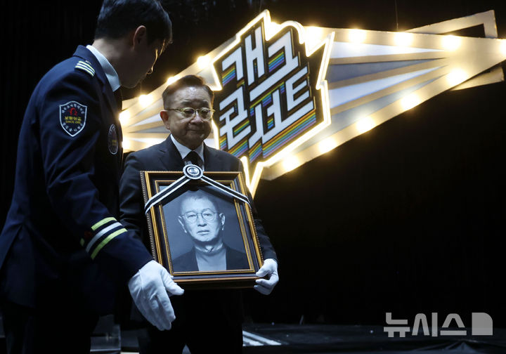 [서울=뉴시스] 홍효식 기자 = 개그맨 고 전유성의 노제가 치러진 28일 오전 서울 영등포구 KBS 공개홀에서 개그맨 이홍렬이 고인의 영정을 들고 개그콘서트 녹화장을 나서고 있다. 2025.09.28. yesphoto@newsis.com