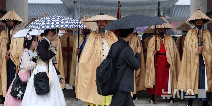 [서울=뉴시스] 추상철 기자 = 가을비가 내린 28일 오전 서울 종로구 광화문 앞에서 외국인 관광객이 조선시대 우비인 유삼과 쓰개를 착용한 수문장 앞을 지나고 있다. 2025.09.28. scchoo@newsis.com