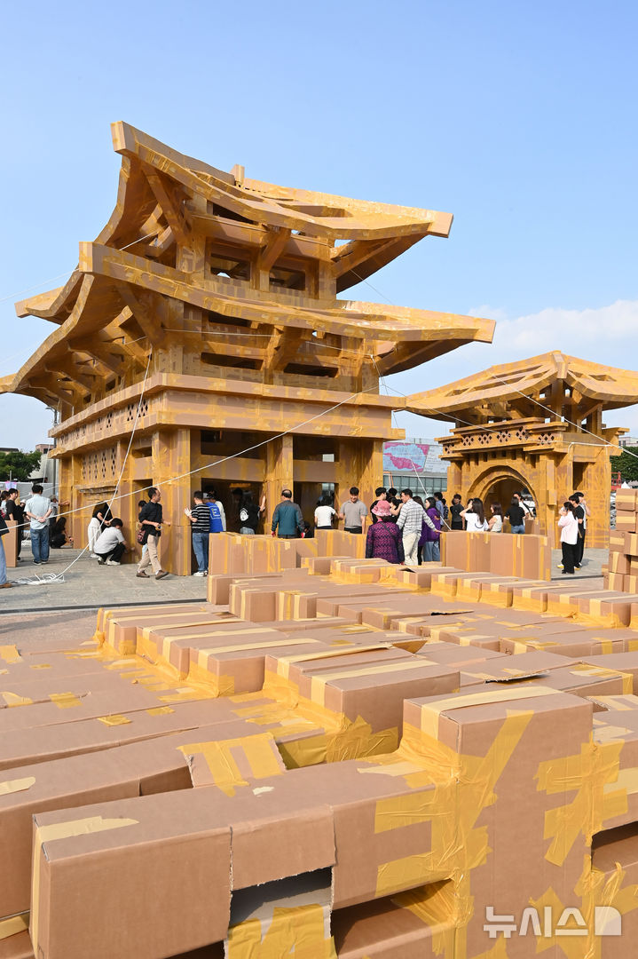 [수원=뉴시스] 김종택 기자 = 제62회 수원화성문화제가 열린 1일 경기 수원시 화성행궁 광장에서 시민들이 종이 박스로 수원화성 팔달문을 제작하고 있다. 종이박스를 자르고 조립하며 제작한 팔달문은 가로와 세로가 각각 18.68m, 13.87m에 높이는 11.73m로 실제 크기의 60% 규모다. 2025.10.01. jtk@newsis.com