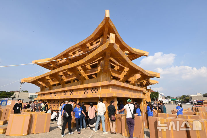 [수원=뉴시스] 김종택 기자 = 제62회 수원화성문화제가 열린 1일 경기 수원시 화성행궁 광장에서 시민들이 종이 박스로 수원화성 팔달문을 제작하고 있다. 종이박스를 자르고 조립하며 제작한 팔달문은 가로와 세로가 각각 18.68m, 13.87m에 높이는 11.73m로 실제 크기의 60% 규모다. 2025.10.01. jtk@newsis.com