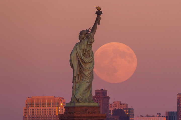 [저지시티=AP/뉴시스] 6일(현지 시간) 미 뉴저지주 저지시티에서 자유의 여신상과 브루클린 스카이라인 뒤로 슈퍼문이 떠오르고 있다. 2025.10.07.