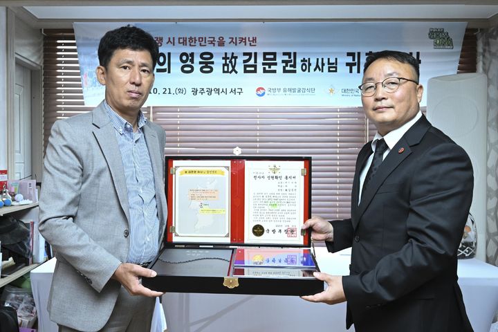 [서울=뉴시스] 조해학 국방부유해발굴감식단장 직무대리(사진 우측)가 故 김문권 하사의 유가족 대표인 친조카 김대중 씨(54)에게 호국의 얼 함을 전달하고 있다. (사진=국방부 제공) 2025.10.21. photo@newsis.com *재판매 및 DB 금지