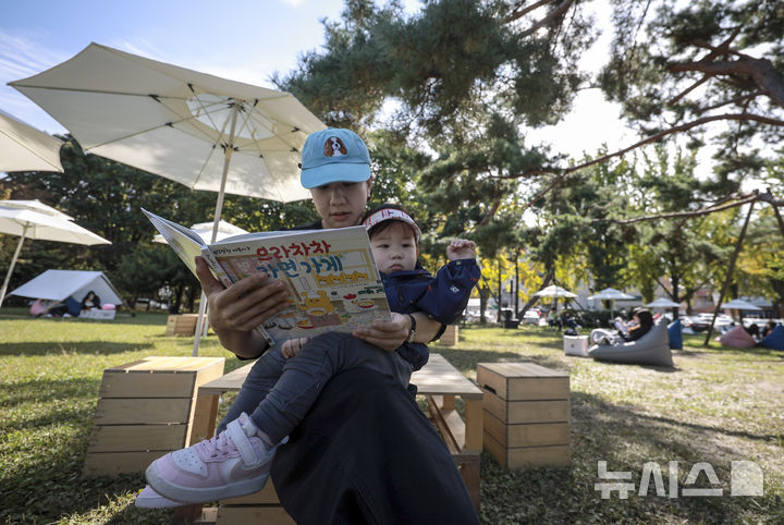 [서울=뉴시스] 정병혁 기자 = 23일 서울 송파구 아시아공원에 마련된 야외도서관을 찾은 시민들이 책을 읽으며 즐거운 시간을 보내고 있다. 송파구청은 가을 독서의 계절을 맞아 동네 공원을 책과 문화가 어우러진 복합문화공간으로 조성해 야외도서관을 운영한다. 2025.10.23 jhope@newsis.com
