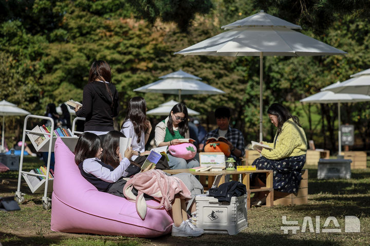 [서울=뉴시스] 정병혁 기자 = 23일 서울 송파구 아시아공원에 마련된 야외도서관을 찾은 시민들이 책을 읽으며 즐거운 시간을 보내고 있다. 송파구청은 가을 독서의 계절을 맞아 동네 공원을 책과 문화가 어우러진 복합문화공간으로 조성해 야외도서관을 운영한다. 2025.10.23 jhope@newsis.com