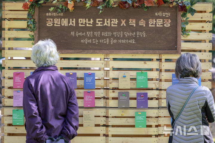 [서울=뉴시스] 정병혁 기자 = 23일 서울 송파구 아시아공원에 마련된 야외도서관을 찾은 시민들이 책 속 한문장을 살펴보고 있다. 송파구청은 가을 독서의 계절을 맞아 동네 공원을 책과 문화가 어우러진 복합문화공간으로 조성해 야외도서관을 운영한다. 2025.10.23 jhope@newsis.com