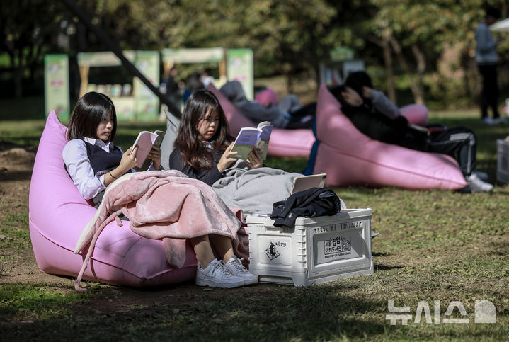 [서울=뉴시스] 정병혁 기자 = 23일 서울 송파구 아시아공원에 마련된 야외도서관을 찾은 시민들이 책을 읽으며 즐거운 시간을 보내고 있다. 송파구청은 가을 독서의 계절을 맞아 동네 공원을 책과 문화가 어우러진 복합문화공간으로 조성해 야외도서관을 운영한다. 2025.10.23 jhope@newsis.com