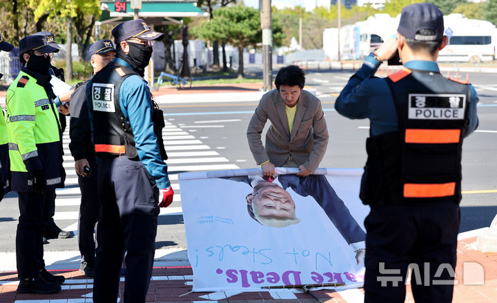 [경주=뉴시스] 이무열 기자 = APEC 정상회의를 사흘 앞둔 28일 경북 경주화백컨벤션센터(HICO) 앞에서 이제석 이제석광고연구소 대표가 트럼프 미국 대통령 얼굴이 담긴 플래카드 퍼포먼스를 하자 경찰에게 제지당하고 있다. 2025.10.28. lmy@newsis.com