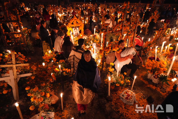 [AP/뉴시스] 멕시코 전통 축일인 '이승을 떠난 자의 날'을 맞아 1일 미초아칸주 내 한 마을묘지에서 가족들이 먼저 세상을 떠난 식구들 묘지 엎에 촛불을 켜고 꽃을 바치며 오랜동안 자리를 지키고 있다 