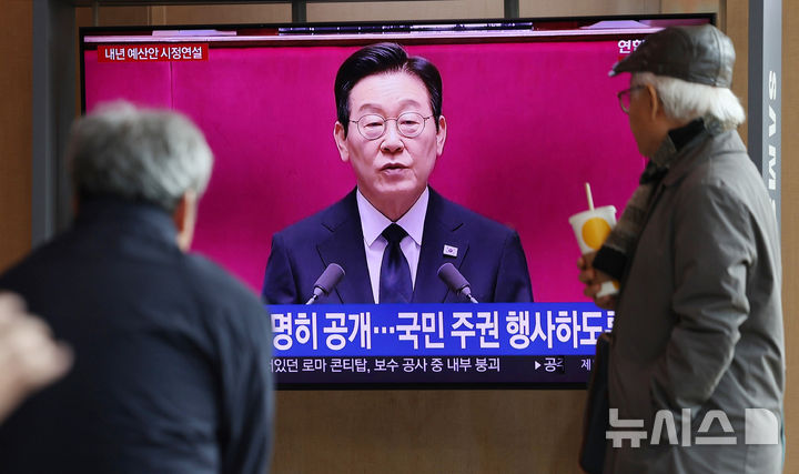[서울=뉴시스] 김진아 기자 = 사진은 지난 4일 서울 중구 서울역에서 시민들이 이재명 대통령의 2026년도 정부 예산안에 대한 시정연설 뉴스를 시청하고 있는 모습. 2025.11.04. bluesoda@newsis.com
