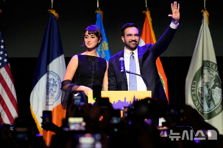 [뉴욕=AP/뉴시스] 미국 뉴욕시장 민주당 후보 조란 맘다니가 4일 당선된 뒤 부인 라마 두와지와 함께 연단에 올라 손을 번쩍 들고 있다.2025.11.06.