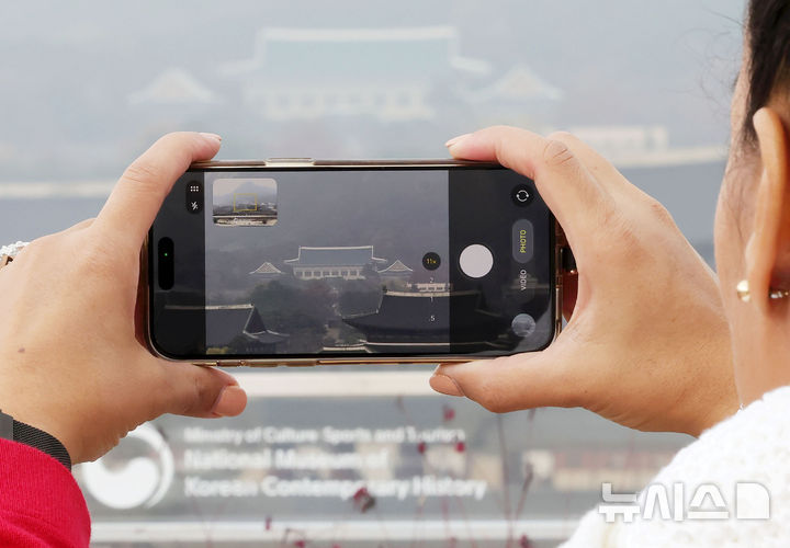 [서울=뉴시스] 홍효식 기자 = 24일 서울 종로구 대한민국역사박물관 옥상정원에서 한 관람객이 청와대를 스마트폰으로 촬영하고 있다.대통령실이 다음 달 중순부터 시설·보안 점검 상태와 부서별 준비 상황에 맞춰 청와대로 순차 이전한다. 대통령실 관계자는 "아직 마무리해야 할 시설·보안 공사 등이 남아 있어 청와대 이전은 12월 둘째주 부터 본격적으로 시작될 것"이라고 23일 밝혔다. 2025.11.24. yesphoto@newsis.com