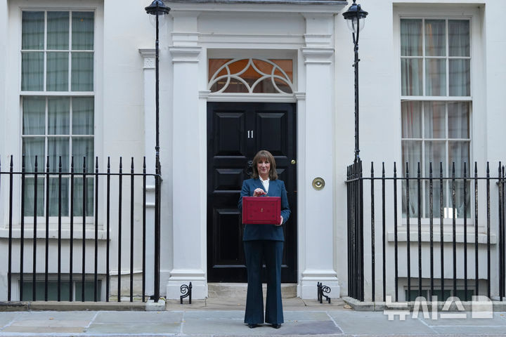 [AP/뉴시스] 영국의 레이첼리브스 재무장관이 26일 내년도 예산안 공개의 연설을 위해 하원으로 출발하기 전 재무장관 관저인 다우닝가 11번지 현관 앞에서 취재진에게 예산안이 든 장관 가방을 들어보이고 있다 
