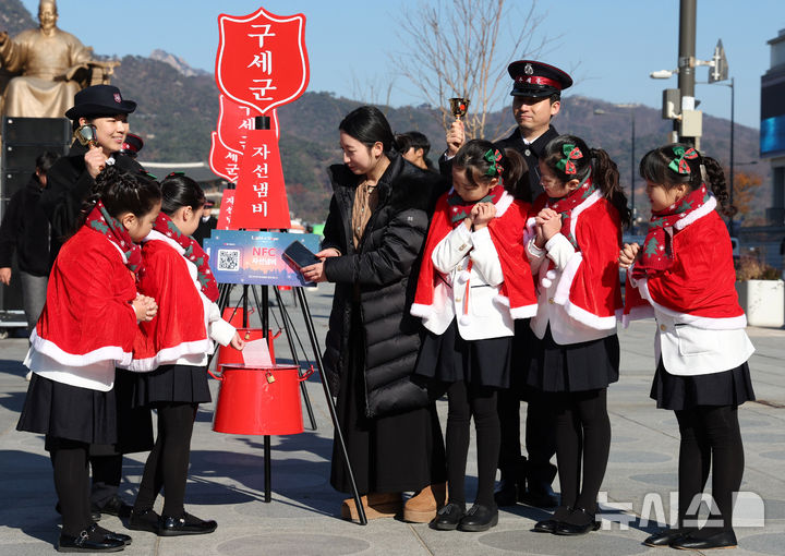 [서울=뉴시스] 추상철 기자 = 28일 오전 서울 종로구 광화문광장에서 열린 '2025 구세군 자선냄비 시종식'에서 서울 주니어 합창단 어린이와 학부모가 현금 및 NFC 자선냄비 모금 시연을 하고 있다. 2025.11.28. scchoo@newsis.com