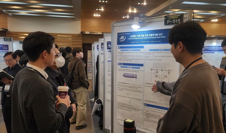 [창원=뉴시스] 강경국 기자 = SNT다이내믹스 박영훈 엔지니어(오른쪽)가 지난달 한국군사과학기술학회 추계학술대회에서 참관객에게 연구논문에 대해 설명을 하고 있다. (사진=SNT다이내믹스 제공). 2025.12.01. photo@newsis.com *재판매 및 DB 금지