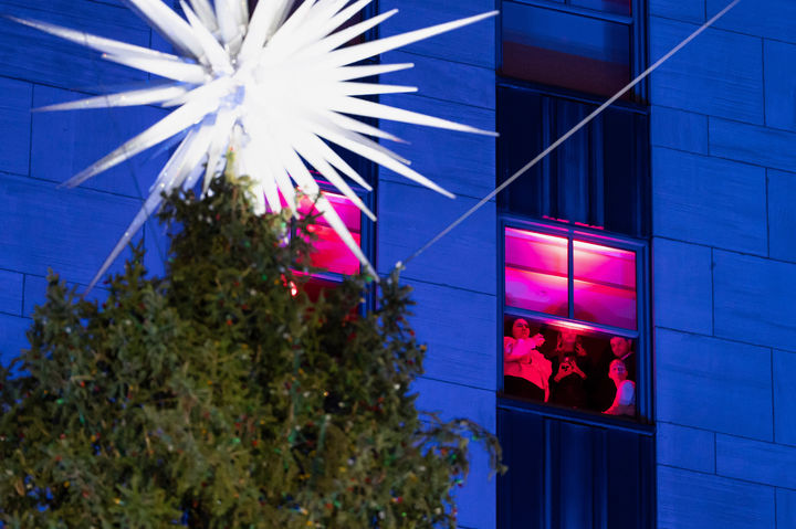 [뉴욕=AP/뉴시스] 3일(현지 시간) 미국 뉴욕 록펠러센터 앞에서 제93회 크리스마스트리 점등식이 열린 가운데 건물 내 사람들이 행사를 지켜보고 있다. 이 크리스마스트리는 지난달 6일 뉴욕주 이스트 그린부시에서 기증받은 노르웨이 가문비나무로 높이 약 23m, 무게 11톤에 달한다. 2025.12.04.