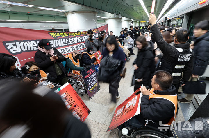 [서울=뉴시스] 이영환 기자 = 전국장애인차별철폐연대(전장연) 회원들이 4일 오전 서울 종로구 지하철5호선 광화문역에서 열린 '제67차 출근길 지하철 탑니다’ 시위를 하는 가운데 시민들이 이동하고 있다. 2025.12.04. 20hwan@newsis.com