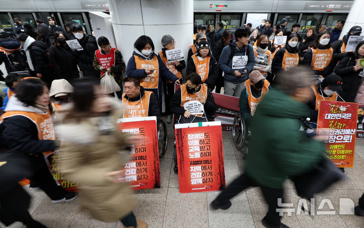 [서울=뉴시스] 이영환 기자 = 전국장애인차별철폐연대(전장연) 회원들이 4일 오전 서울 종로구 지하철5호선 광화문역에서 열린 '제67차 출근길 지하철 탑니다’ 시위를 하는 가운데 시민들이 이동하고 있다. 2025.12.04. 20hwan@newsis.com