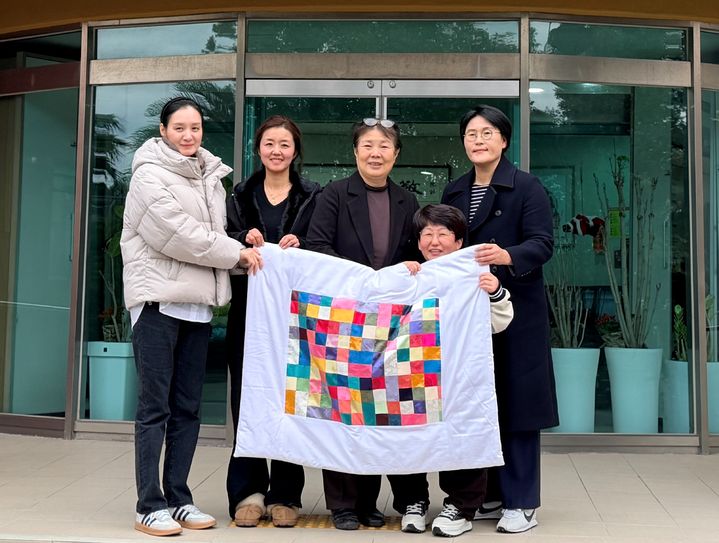 [제주=뉴시스] 4일 치유공예그룹 '손의기억'과 제주문화예술재단 관계자가 제주시 한경면에 위치한 미혼모센터 애서원에 아기이불 10채를 기증하고 있다. (사진=제주문화예술재단 제공) 2025.12.05. photo@newsis.com *재판매 및 DB 금지