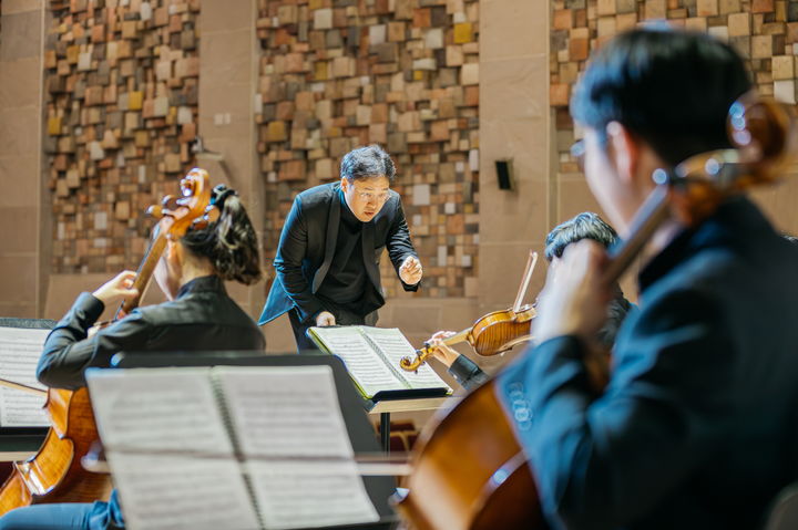 [서울=뉴시스] 알레그로 오케스트라 단원들이 사이에서 윤염광 감독이 연주를 지휘하는 모습. (사진=KB국민카드 제공) 2025.12.10. photo@newsis.com *재판매 및 DB 금지