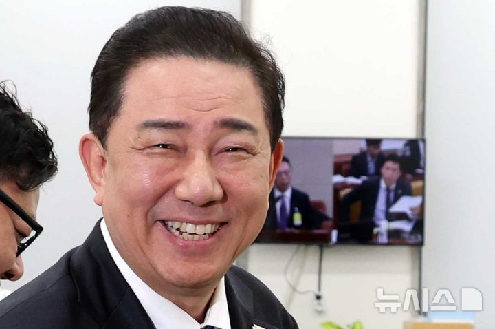 [서울=뉴시스] 조성봉 기자 = 김병기 더불어민주당 원내대표가 17일 오후 서울 여의도 국회 원내대표실에서 취재진을 향해 미소짓고 있다. 김 원내대표 너머로 쿠팡 침해사고 관련 청문회가 생중계 되고 있다. 2025.12.17. suncho21@newsis.com