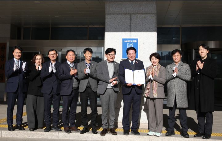 [안양=뉴시스] 최대호 경기 안양시장(오른쪽 네번째)이 18일 시청 본관 정문 기둥에 스마트도시 현판을 달고 인증서를 들고 직원들과 기념촬영을 하고 있다. (사진=안양시 제공) 2025.12.18. photo@newsis.com *재판매 및 DB 금지