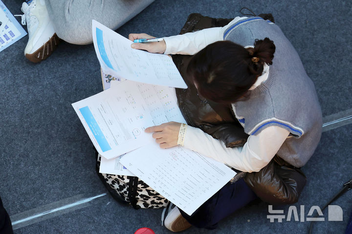 [서울=뉴시스] 홍효식 기자 = 18일 서울 강남구 코엑스에서 열린 2026학년도 정시 대학입학정보박람회를 찾은 학부모가 입장하기 위해 앉아 기다리며 자료를 살펴보고 있다. 2025.12.18. yesphoto@newsis.com