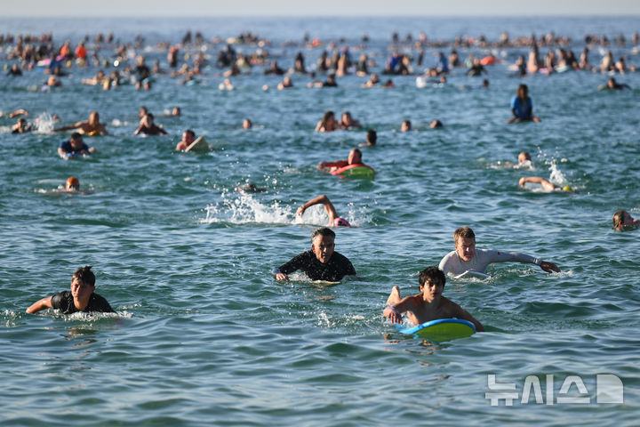 [시드니=AP/뉴시스] 19일(현지 시간) 호주 시드니 본다이비치 앞 바다에서 서퍼와 수영객들이 지난 14일 발생한 총격 희생자들을 추모하는 헌정 수영 행사에 참여하고 있다. 2025.12.19.