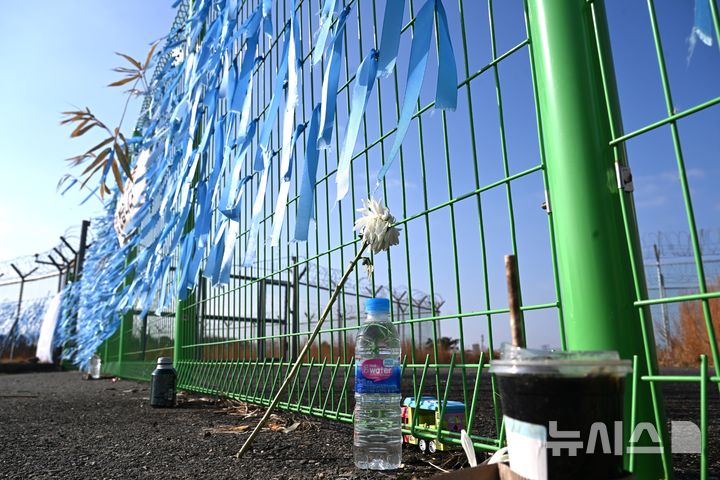 [무안=뉴시스] 이현행 기자 = 제주항공 무안공항 참사 1주기를 앞둔 지난 15일 오전 전남 무안군 무안국제공항 활주로 인근에 희생자를 추모하는 하늘색 리본과 국화, 물, 커피 등이 놓여있다. 2025.12.15. lhh@newsis.com