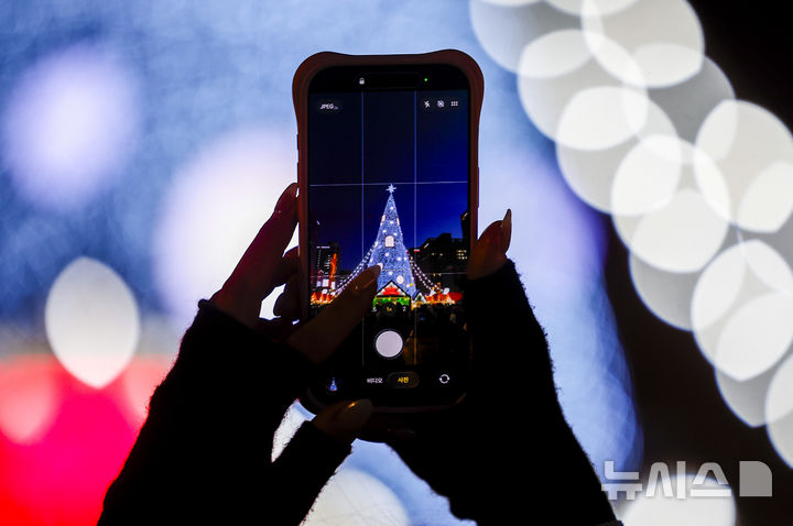 [서울=뉴시스] 정병혁 기자 = 21일 서울 종로구 광화문광장에서 열린 광화문 마켓을 찾은 시민이 크리스마스 트리 사진을 찍고 있다. 2025.12.21. jhope@newsis.com